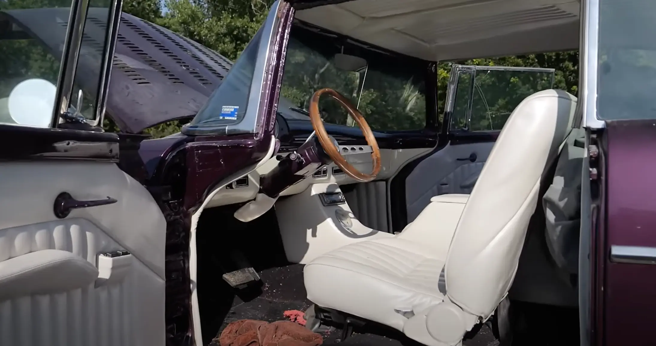 Interior view of Pole Barn Garage’s 1955 Ford Fairlane featuring white upholstery, a wooden steering wheel, and classic detailing