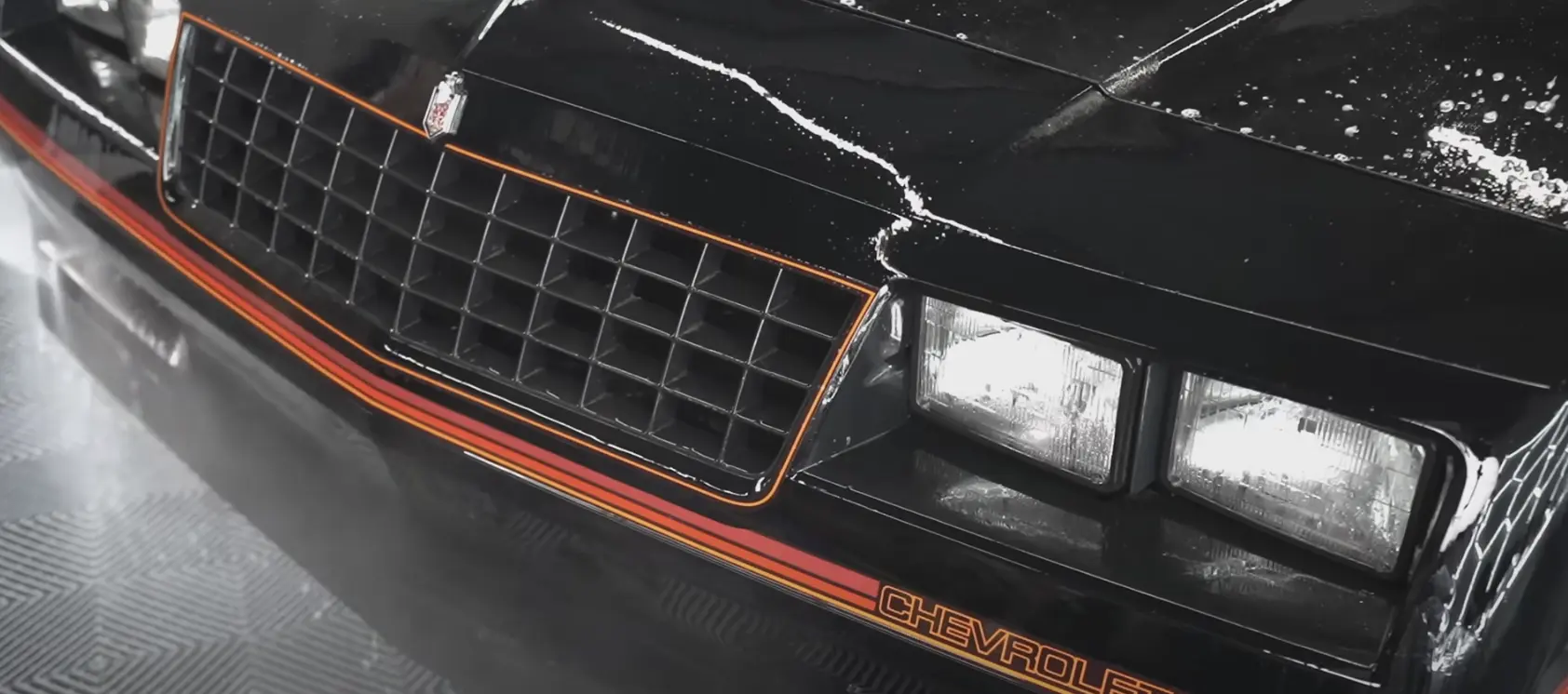 Close-up of a 1985 Monte Carlo SS grille and headlights, showcasing its restoration with a sleek black finish and orange accents