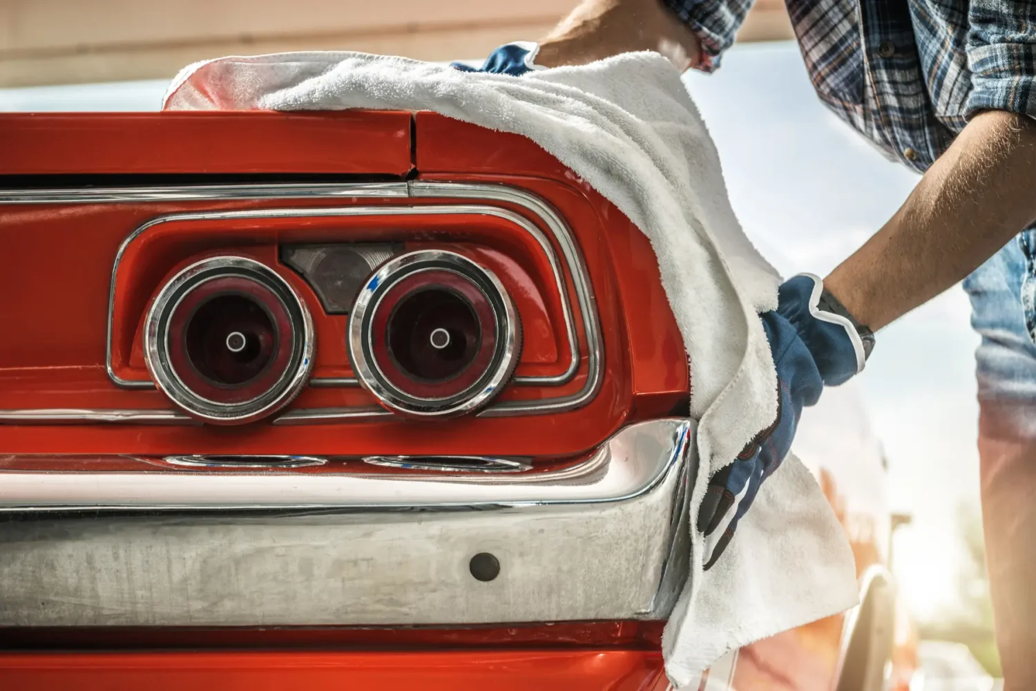 A Beginners Guide to Restoring Classic Cars 3 - JC Whitney Person polishing the rear chrome and taillights of a vintage red car with a cloth