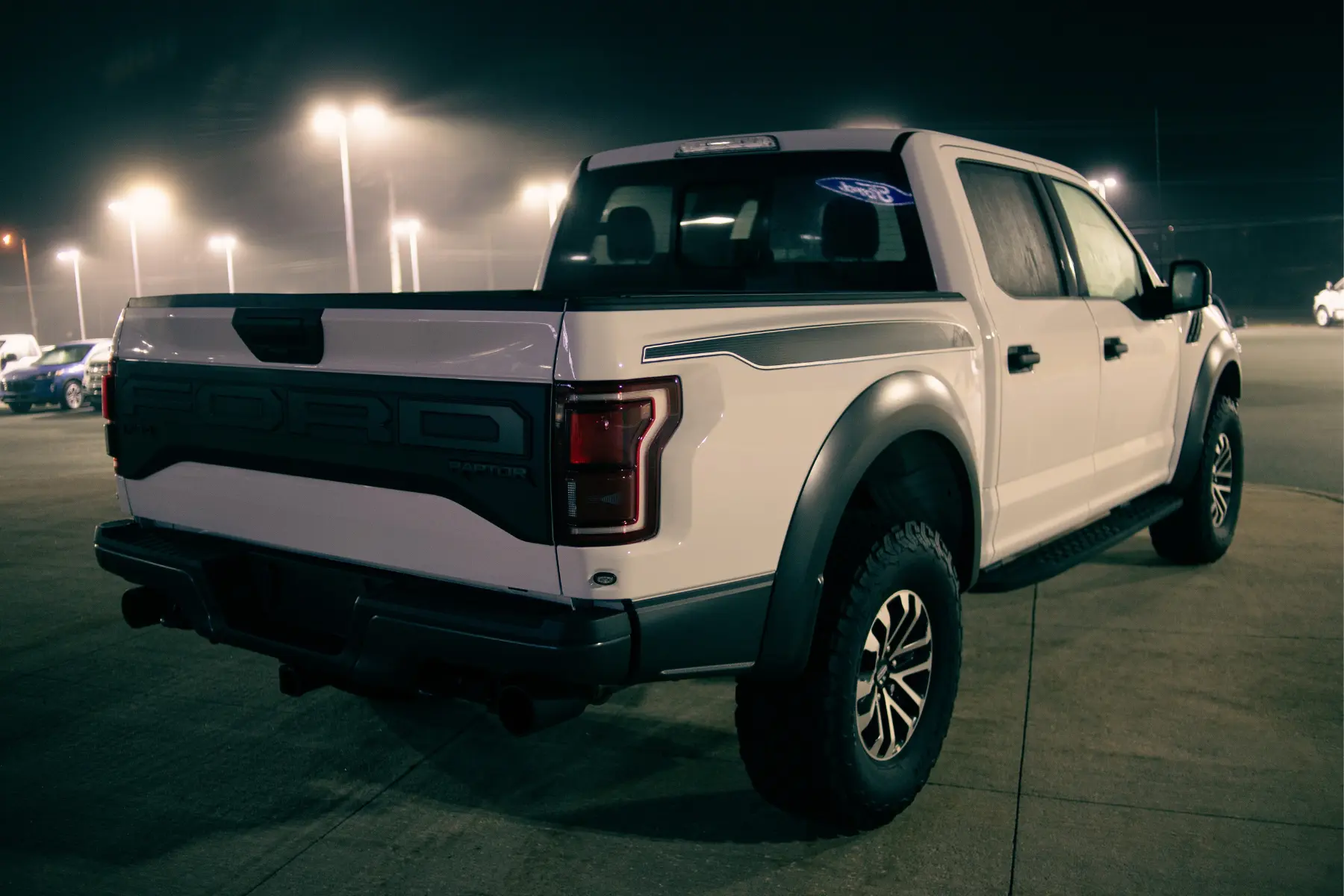 F150 suspension lift kit installed on a white Ford Raptor parked under bright lights in a dealership lot at night