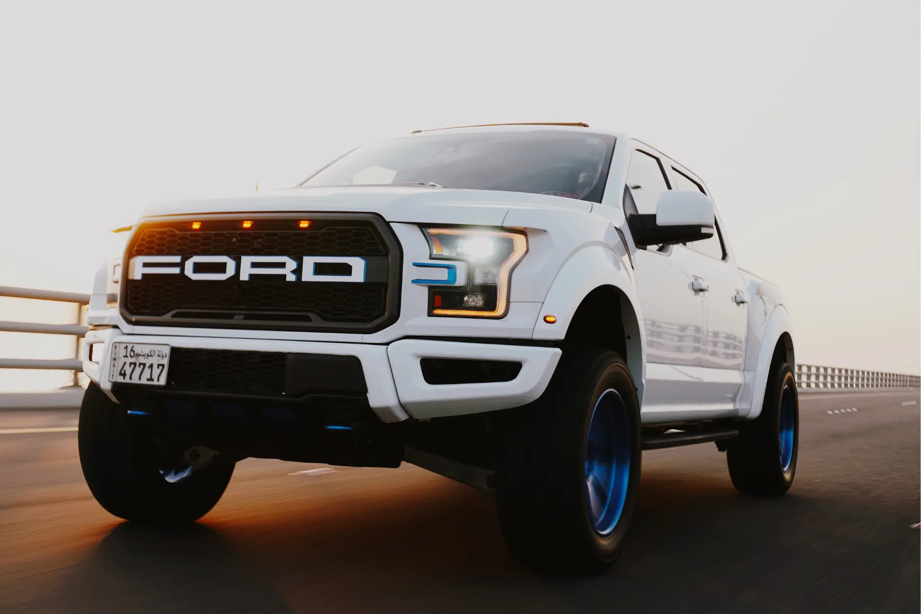 Ford truck suspension upgrades with wide tires and custom wheels driving on a highway at sunset