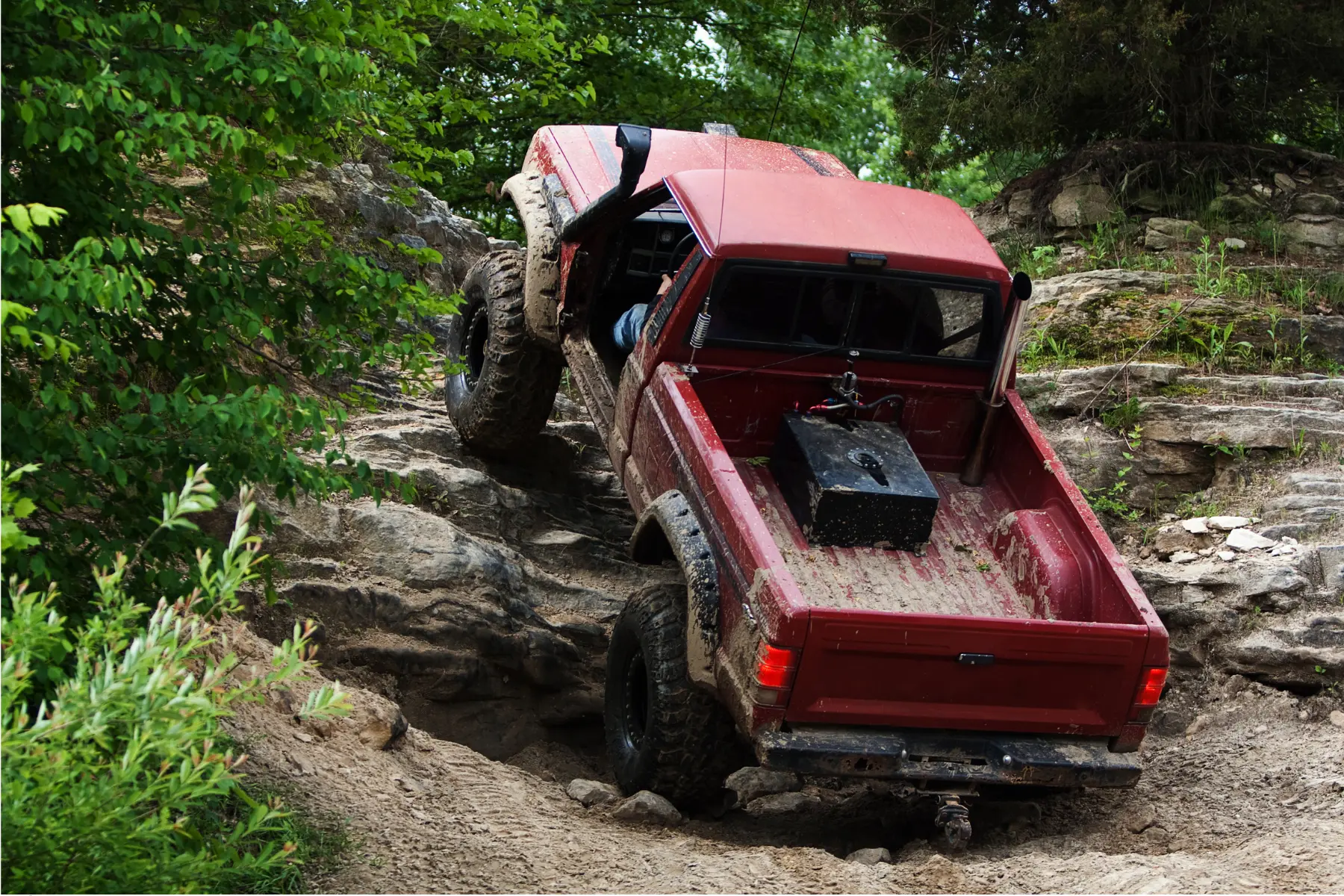 Lift kits for off-roading help a red truck climb a steep, rocky trail covered in mud and rugged terrain.