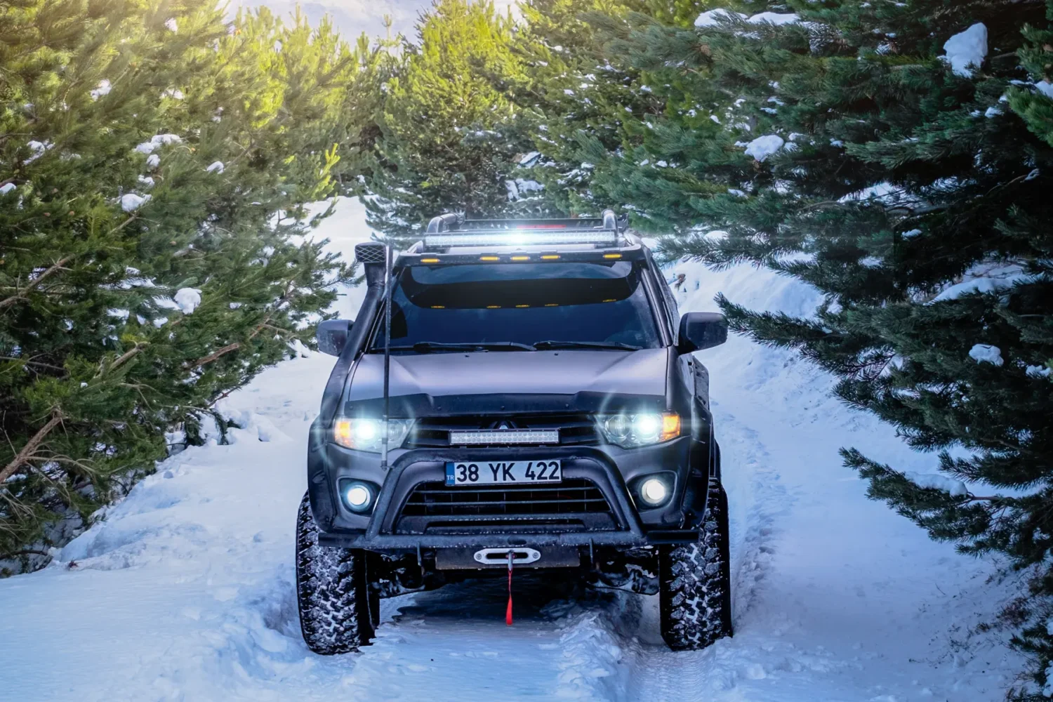 lift kits for trucks - JC Whitney Lift kits for trucks enhance this black off-road vehicle navigating a snowy mountain trail surrounded by evergreen trees.