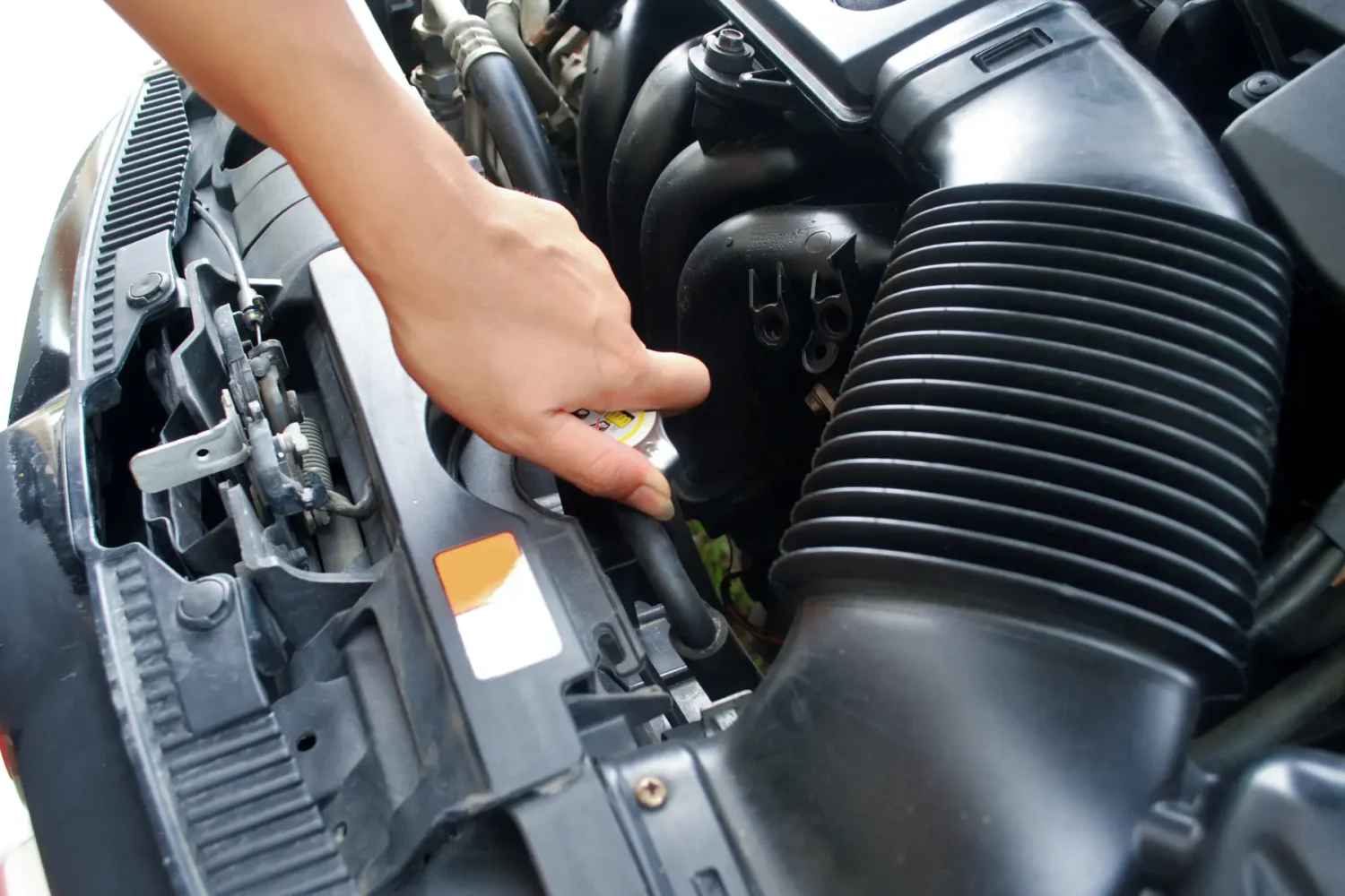 Car Cooling System Maintenance - JC Whitney Car cooling system being checked by hand near the radiator cap under the hood.