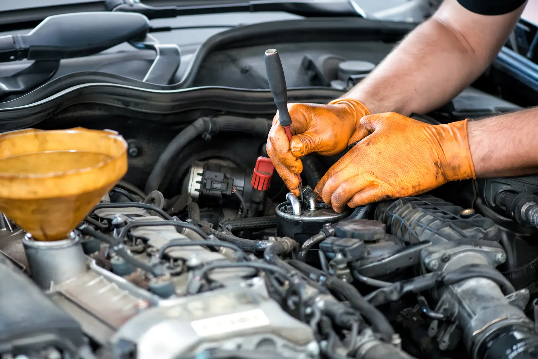 Car maintenance technician using a screwdriver while working on engine components under the hood.