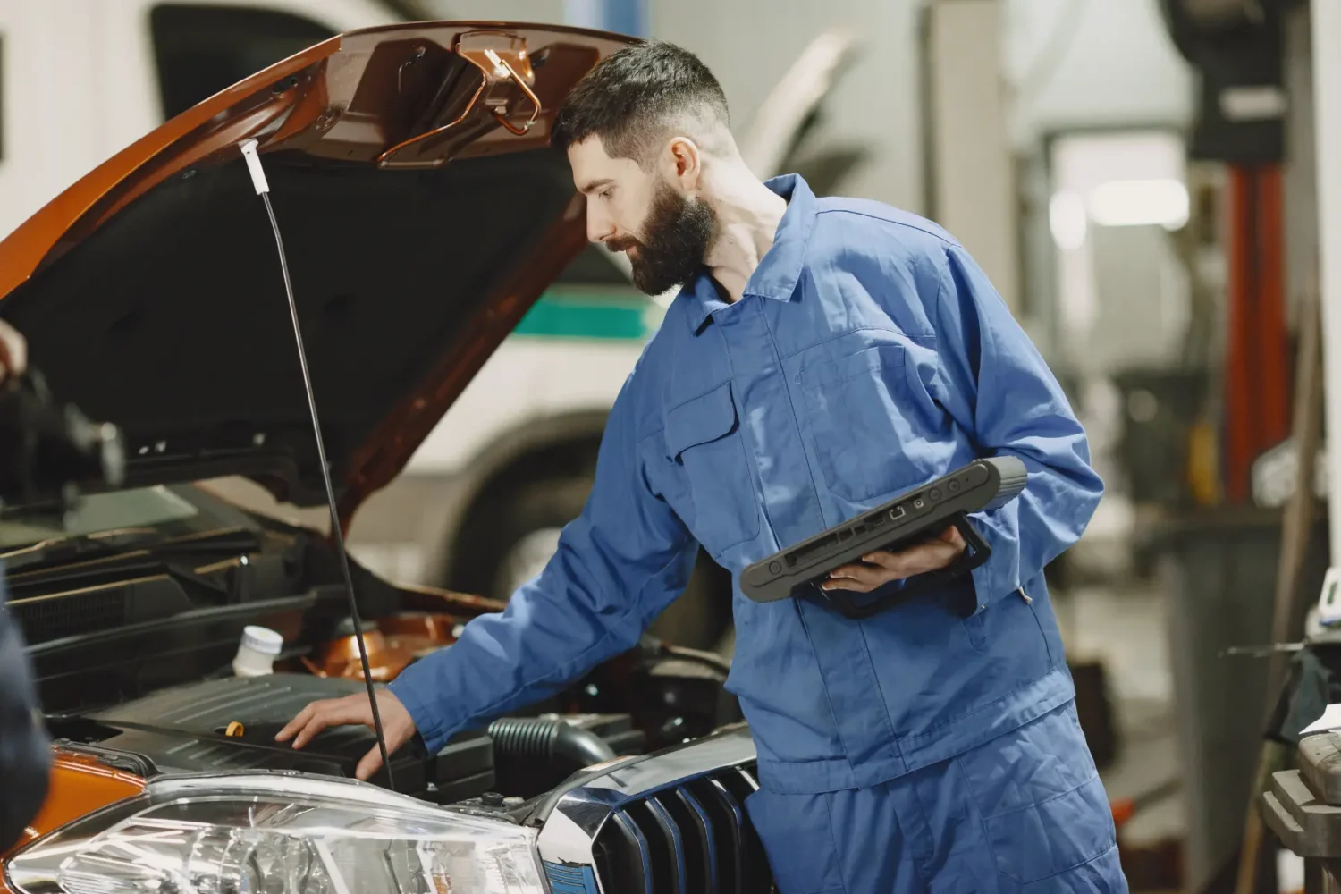 Car Tune-Ups - JC Whitney Car tune-ups technician inspecting engine components with a diagnostic tablet in a garage.