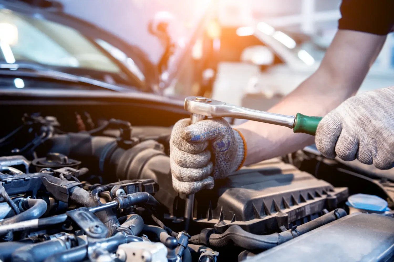 car engine boost systems - JC Whitney Car engine boost systems mechanic tightening a bolt inside an open engine bay with a ratchet tool.