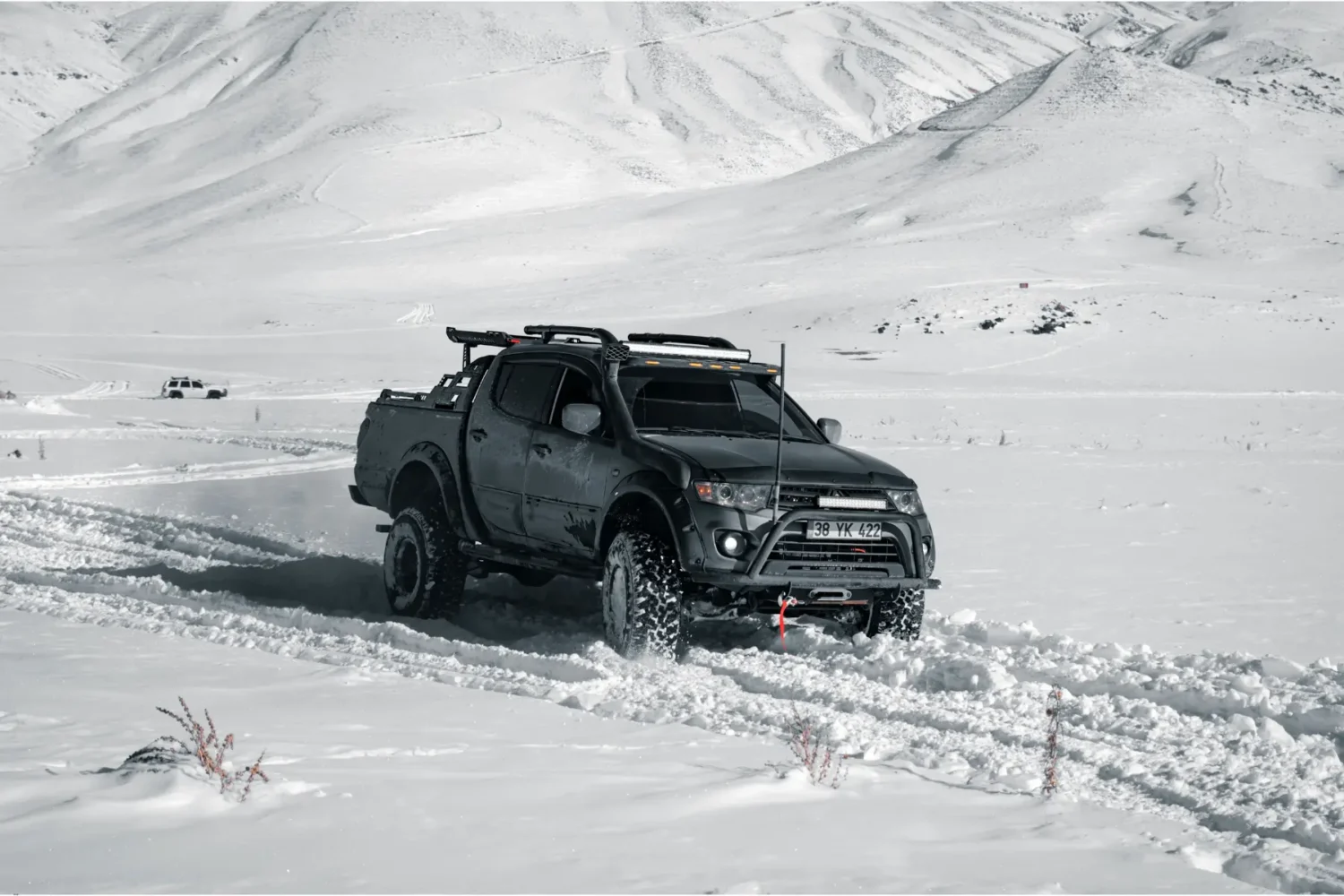 custom truck suspension - JC Whitney Custom truck suspension supporting a black lifted pickup navigating deep snow in mountainous terrain.