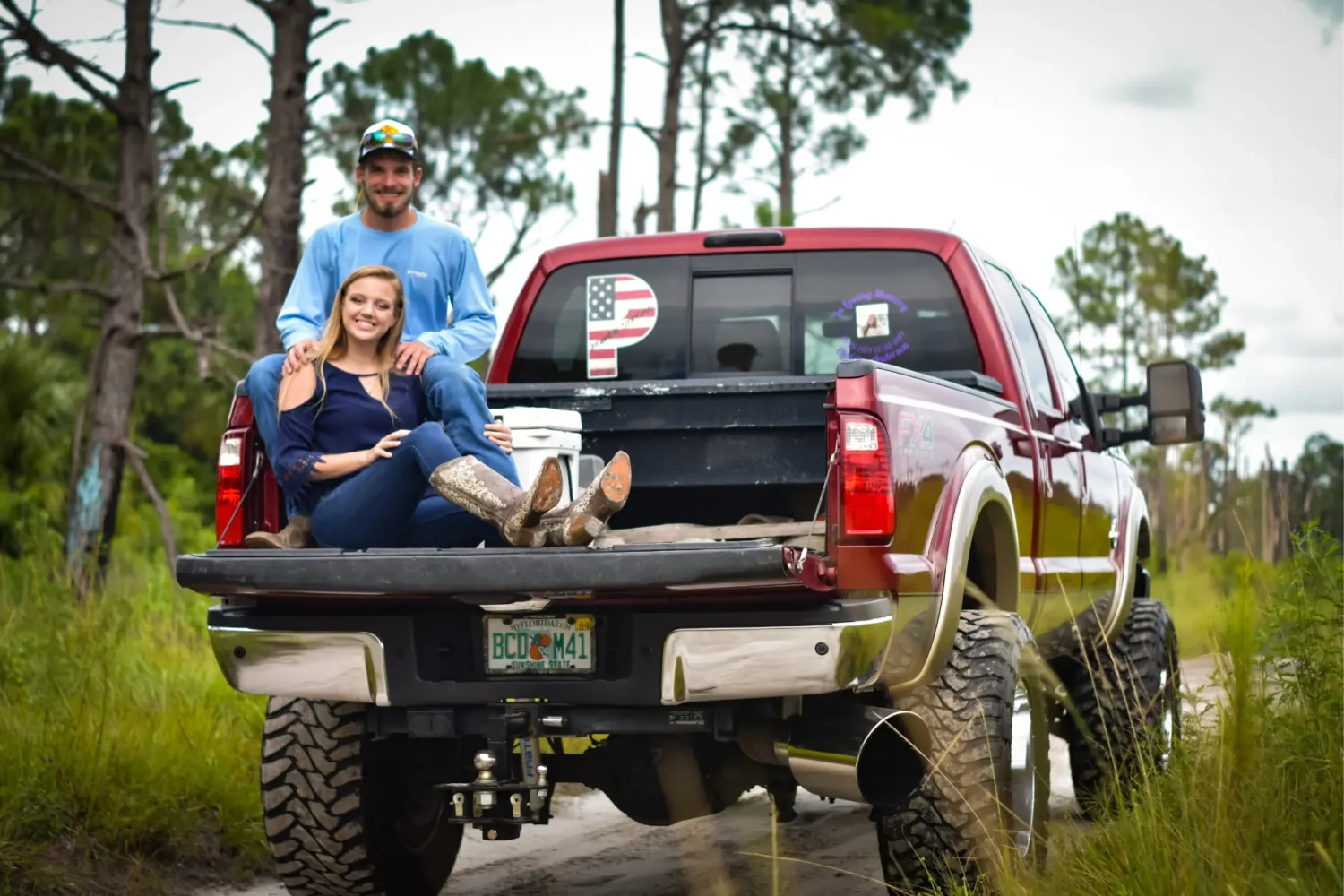 lifted truck suspension - JC Whitney Lifted truck suspension shown on a red pickup with large tires and couple sitting on the tailgate.