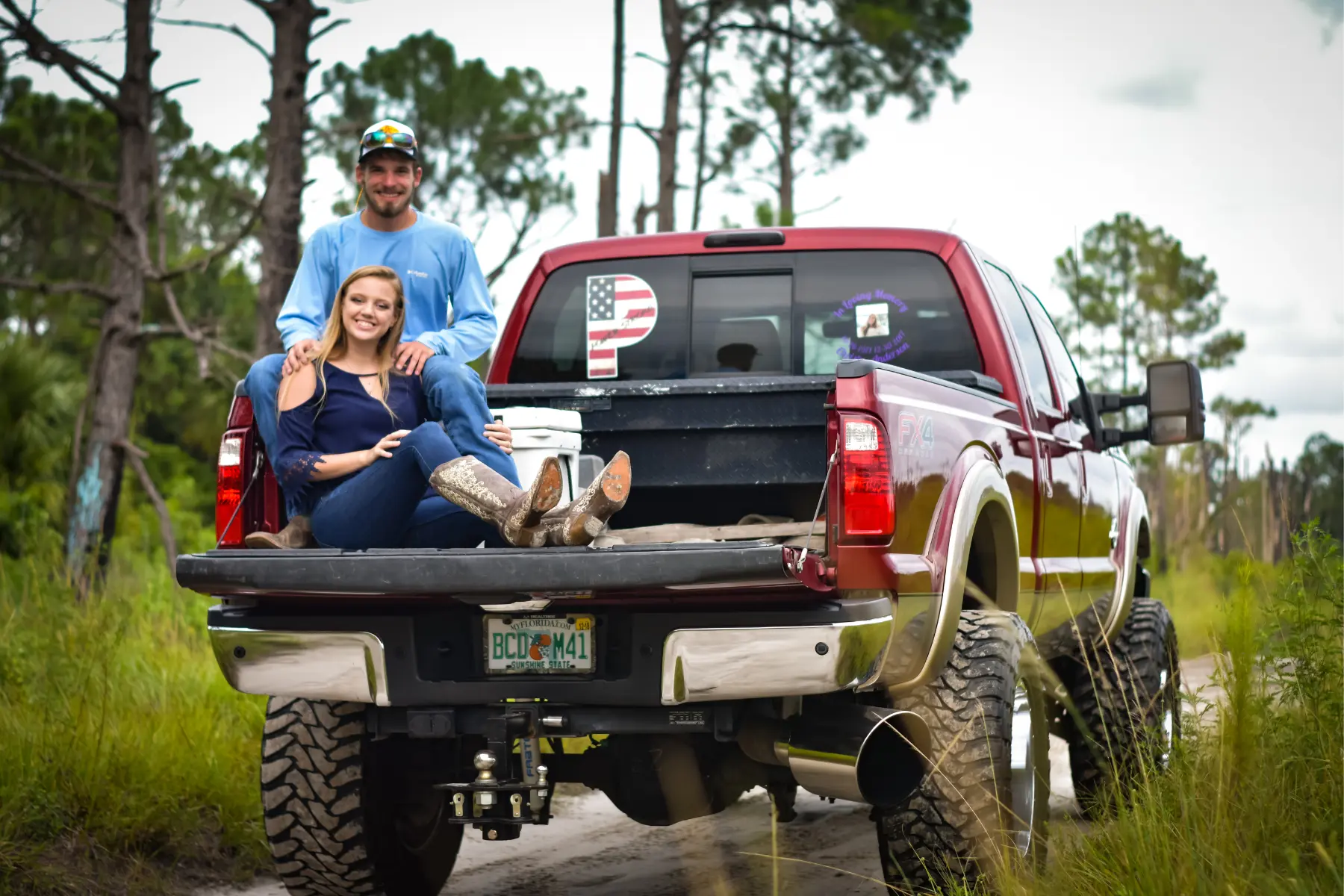 Lifted truck suspension shown on a red pickup with large tires and couple sitting on the tailgate.
